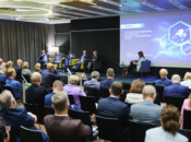 Panel konferencyjny z pięcioma prelegentami siedzącymi na scenie, jedną osobą moderującą i dużą publicznością siedzącą naprzeciwko nich. Na ekranie wyświetlana jest cyfrowa grafika i tekst w języku polskim. Pokój jest jasno oświetlony i nowoczesny, a ludzie ubrani są w stroje biznesowe.